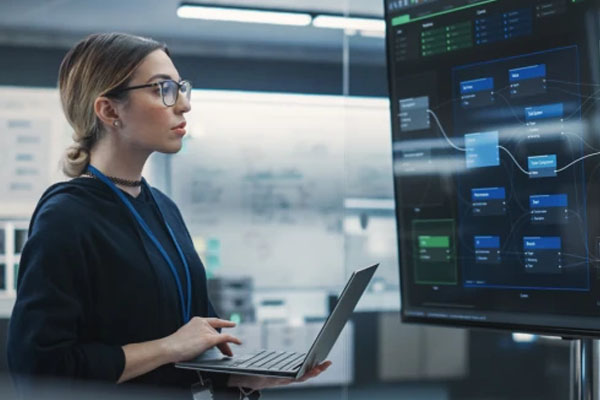 Lady holding laptop looking at monitor
