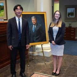 Business student Benjamin Fu BBA ’26 and law student Morgan Hovan J.D. ’27 pose with the portrait of the late Alvin P. Anderson at TowneBank. Photo: David F. Morrill