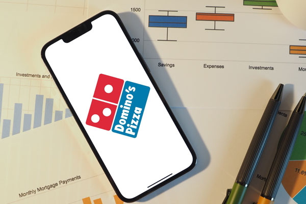 dominos app on phone placed on financial reports and pens