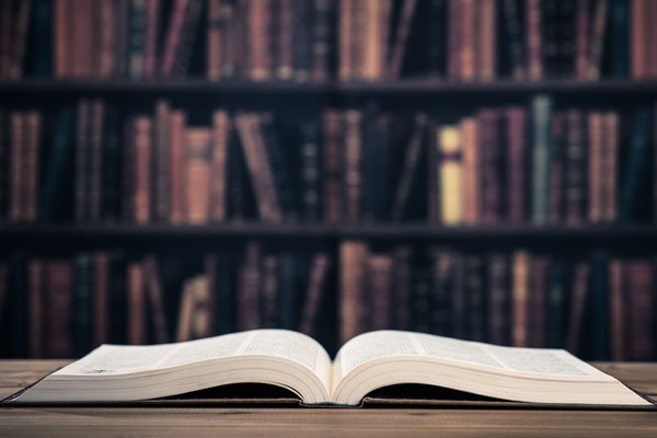 open book on table with bookshelf in background